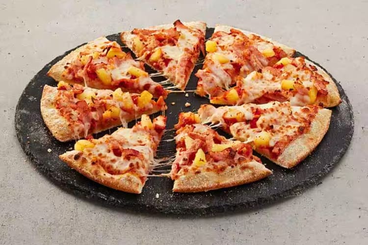 A Hawaiian pizza from Domino's on a black serving board