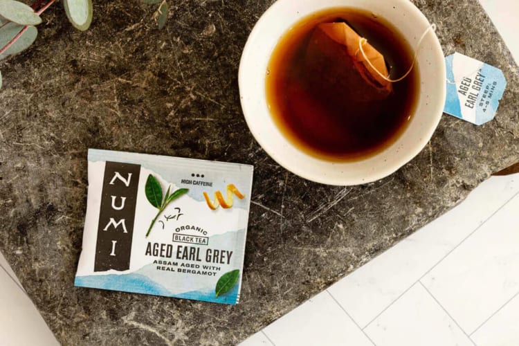 A mug of tea next to a sachet of Numi Earl Grey tea, one of the best Earl Grey teas