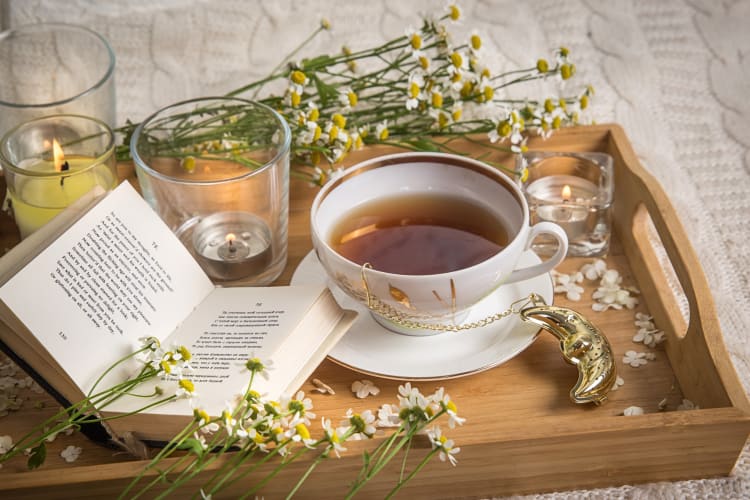 A mug of tea surrounded by a book, candles and flowers
