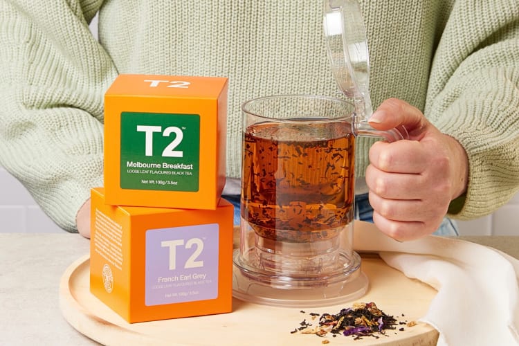 A hand holding a mug of tea next to two boxes of T2 tea