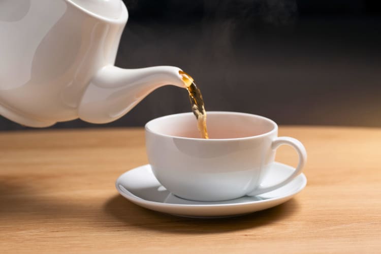 Pouring hot tea into a white cup.