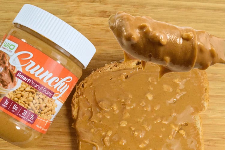 A bottle of WiO SmartFoods Crunchy Peanut Butter next to a slice of bread with peanut butter on