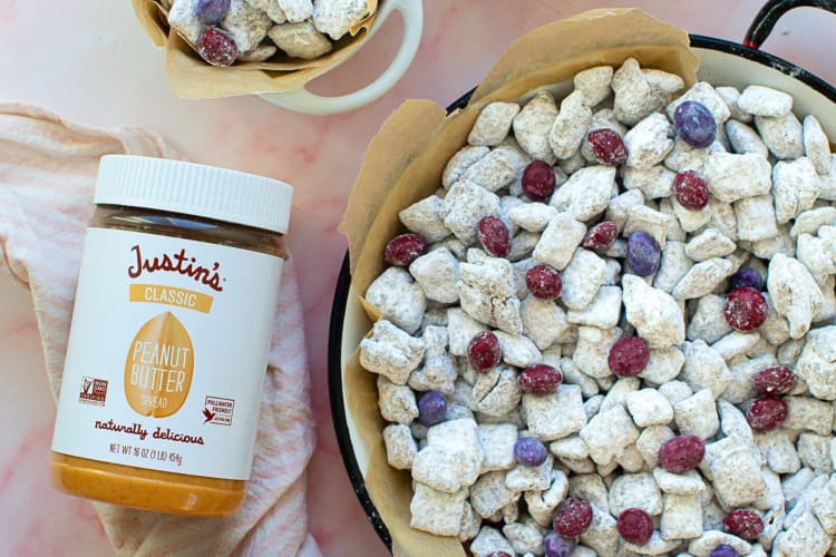 A bottle of Justin’s Classic Peanut Butter next to a bowl of peanut snacks