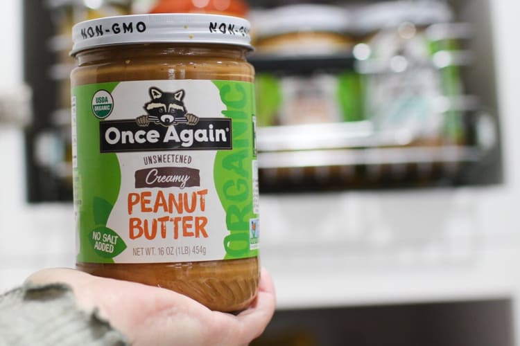 A hand holding a bottle of Once Again Organic Creamy Peanut Butter