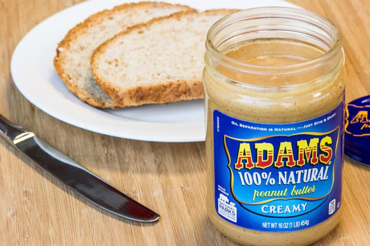 A bottle of Adam’s 100% All-Natural Peanut Butter in front of bread slices