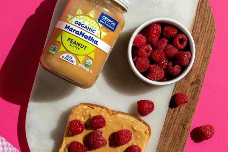 A bottle of Maranatha peanut butter with a bowl of raspberries and a slice of toast