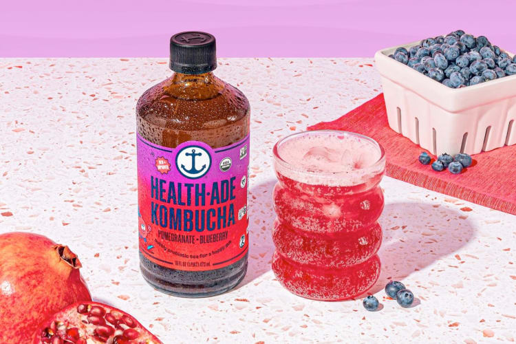A bottle of Health-Ade kombucha next to fresh blueberries and pomegranate