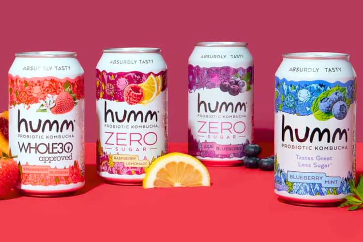 Four cans of different flavored Humm kombucha next to fresh fruits