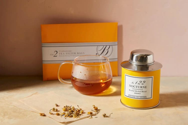 A glass mug of tea in between a packet and a tin of Bellocq tea