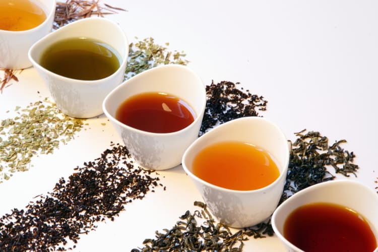 Different rows of loose-leaf teas in rows with mugs of tea on top of each