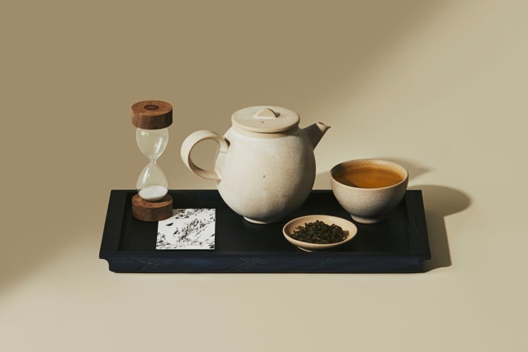 A pot, a mug, tea leaves, a card and a sand timer on a serving tray