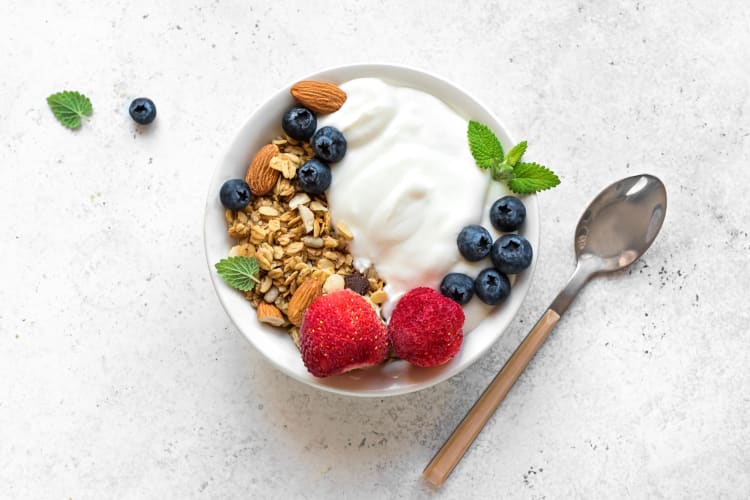 A spoon and a bowl of yogurt topped with granola and berries