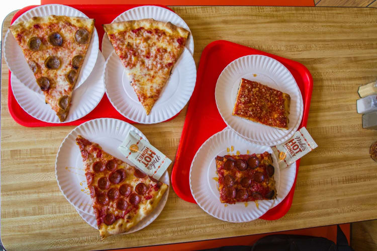 Individual slices of pizza on white paper plates with packets of hot honey.