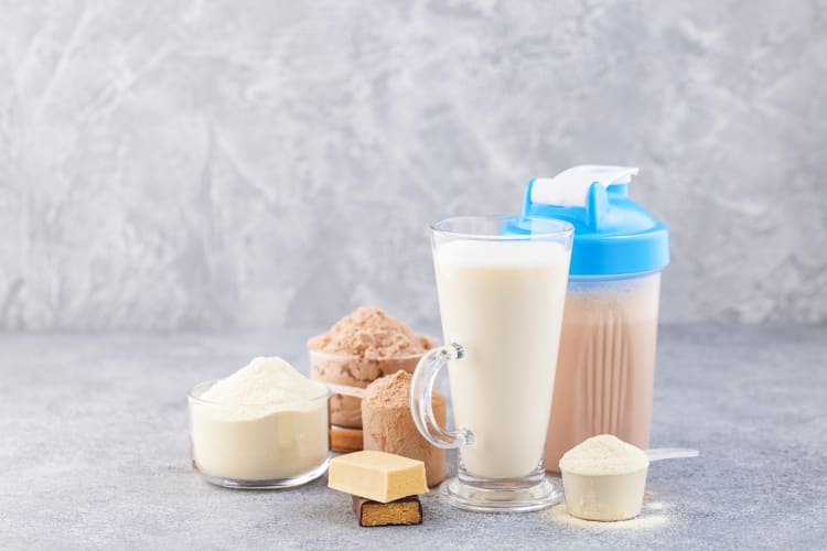 A shaker, scoops of protein powder, a glass of milk and chocolate bars