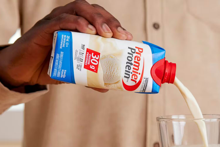 A hand pouring Vanilla Premier protein from a carton into a glass