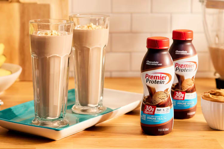 Two bottles of Chocolate Premier Protein next to two chocolate smoothies
