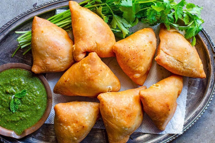 Aerial view of eight samosas, cilantro and a bowl of sauce, from Spice Symphony