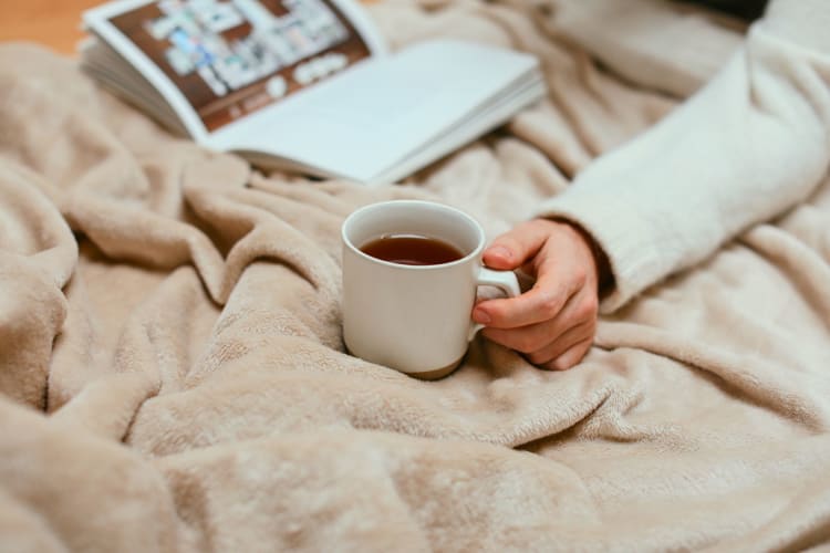 Young woman holding a cup of tea in bed.