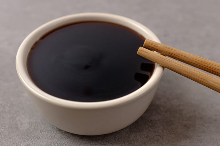 A white bowl of teriyaki sauce with chopsticks resting on it