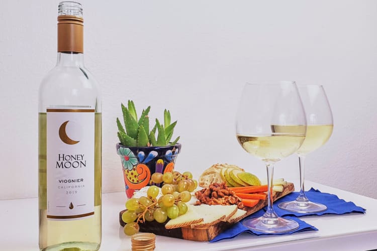 A bottle and two glasses of Honey Moon Viognier with cheeseboard foods in between them