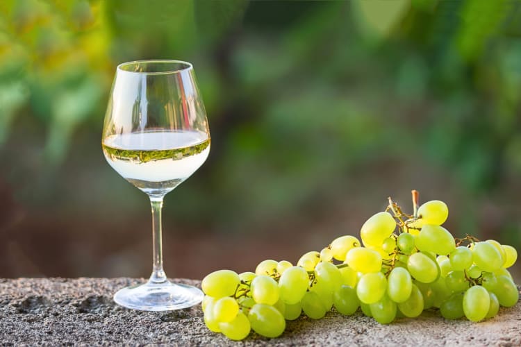 A glass of white wine next to a bunch of grapes