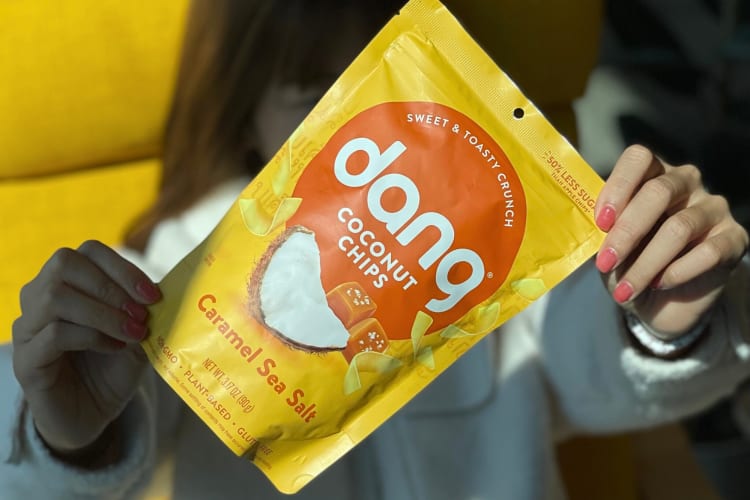 Hands holding a packet of Dang Coconut Chips