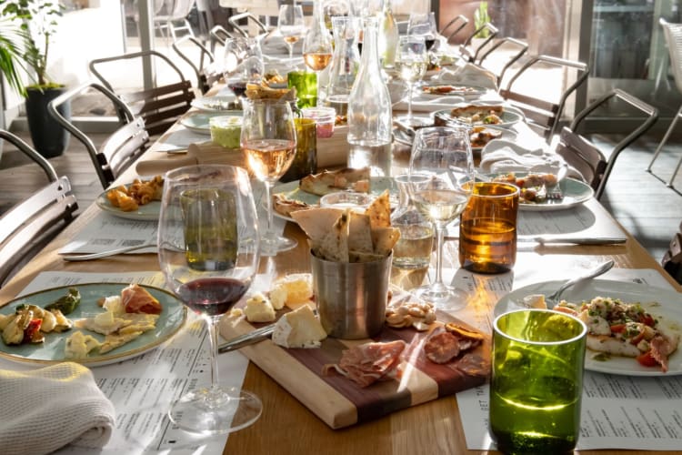 a table laden with wine glasses, charcuterie, pizzas and other foods