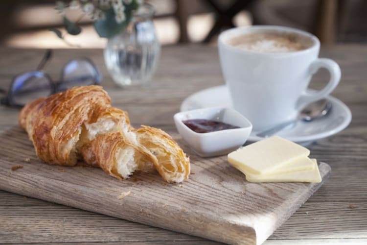 Croissant with butter and jam beside a coffee