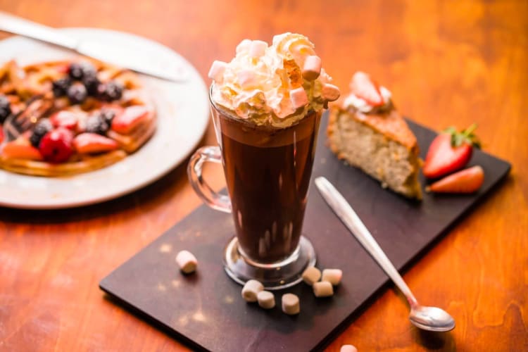 A hot chocolate with a fruit-topped waffle in the background is a popular breakfast in Bath