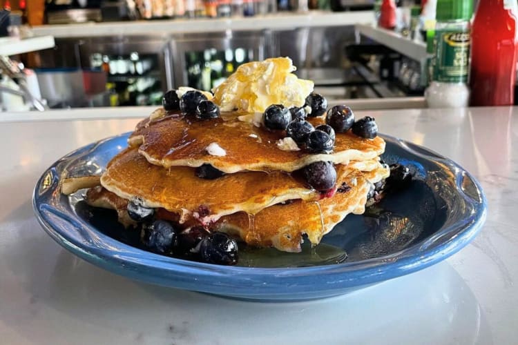 Blueberry pancakes topped with butter, maple syrup and fresh bluberries