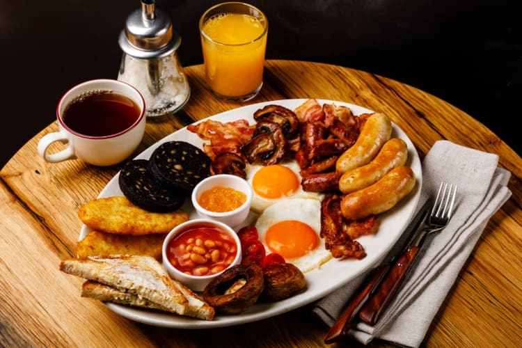 A full Irish breakfast on a plate comprising, sausages, bacon, egg, beans, black pudding, mushrooms and tomatoes