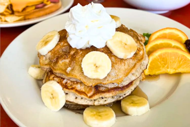 Pancakes with banana and cream on a plate with oranges