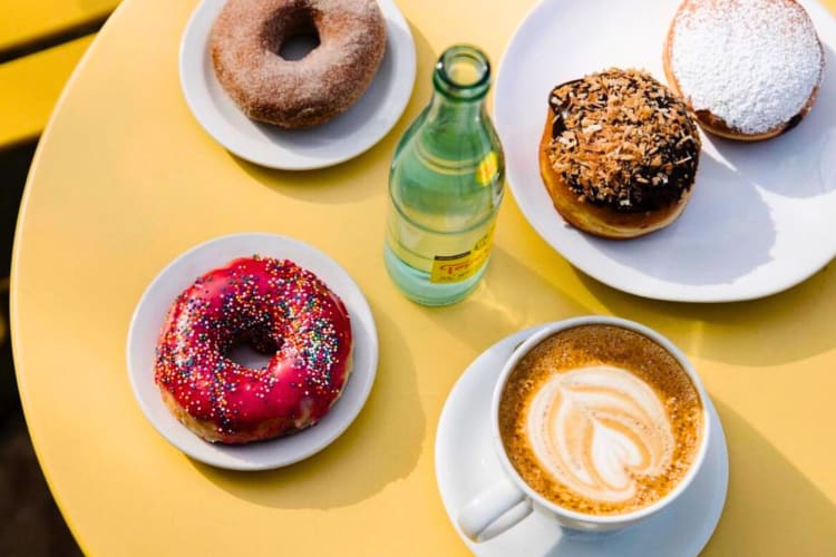 Donuts, a coffee and a glass water bottle on a yellow table