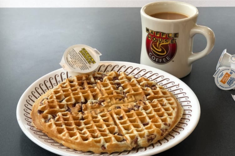 A waffle on a plate next to a mug of coffee