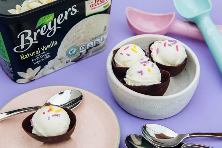 A tub of Breyers ice cream next to a plate and bowl with scoops of ice cream