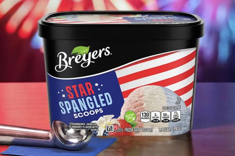 An ice cream scoop in front of a tub of Star Spangled Scoops Breyers ice cream