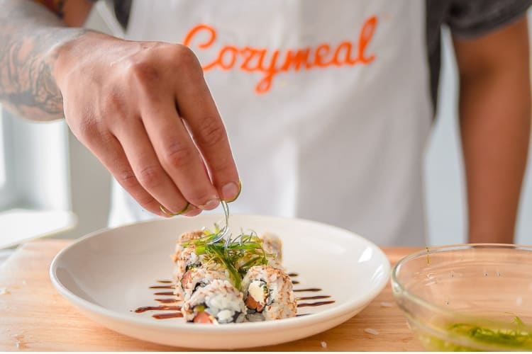 A chef preparing sushi and topping it with seaweed salad