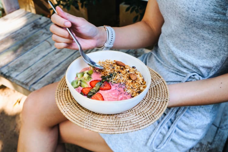 Woman eating smoothie bowl wondering 