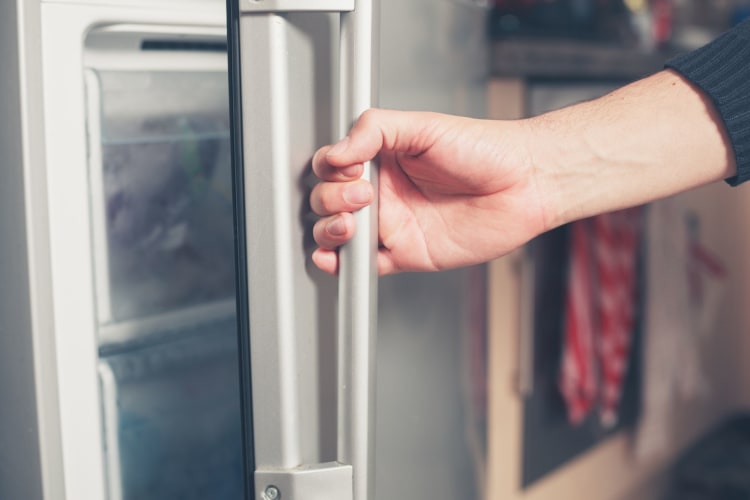 A hand opening a freezer door.