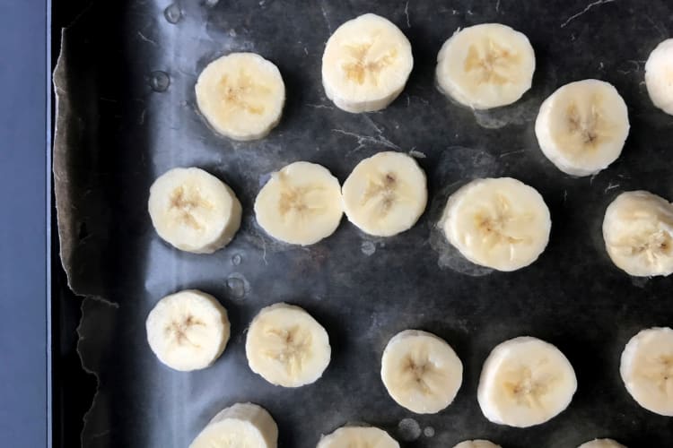 Sliced bananas being freezed with parchment paper