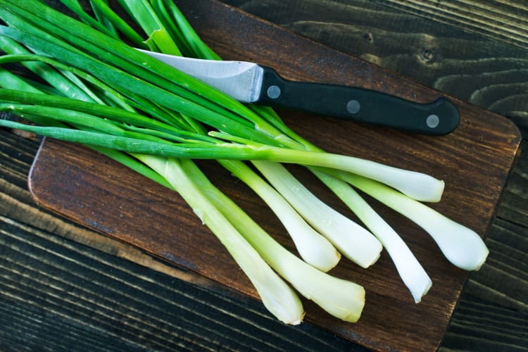 Green onions and a knife on a chopping board.