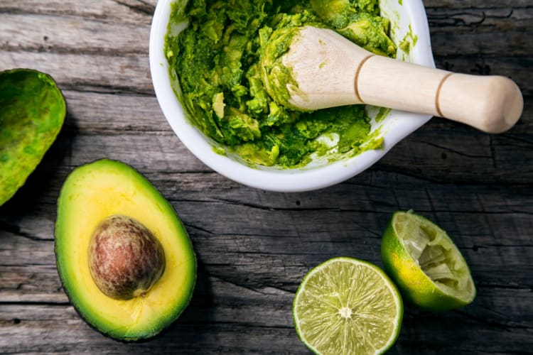 Guacamole in a pestle and mortar next to limes and avocados