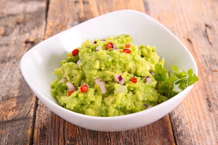 A bowl of guacamole on a wooden surface