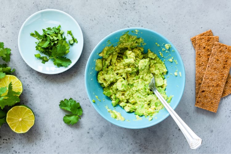 A bowl of guacamole next to other ingredients