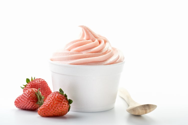 Strawberry frozen yogurt on a ceramic plate with strawberries and a wooden spoon