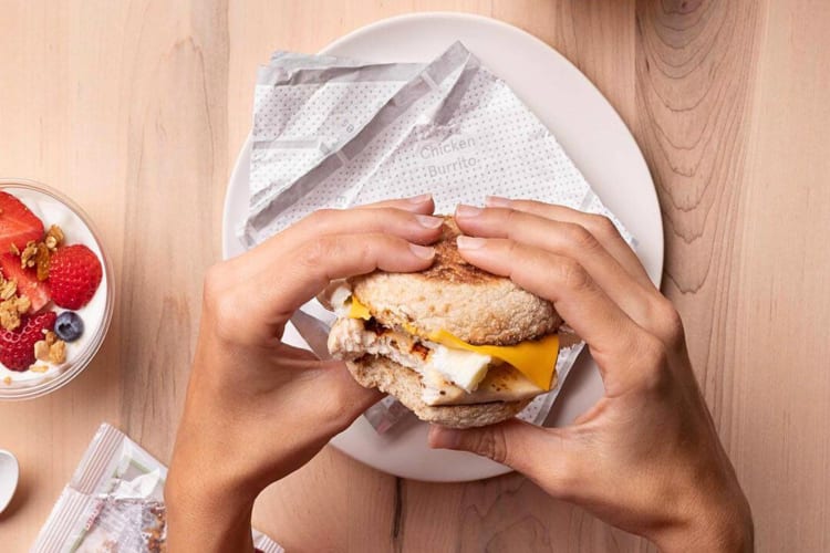 Hands holding a breakfast muffin from Chick-fil-A above a plate