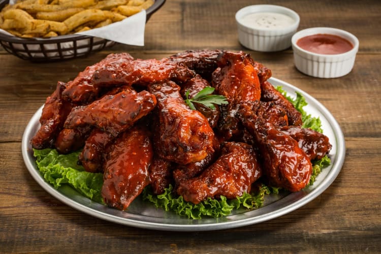 Chicken wings covered in sauce, on a bed of lettuce