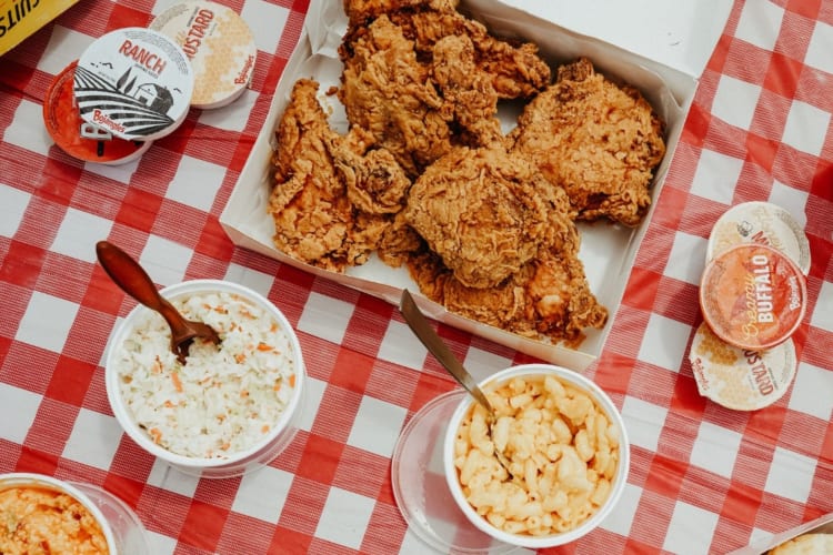 A feast of chicken, fries and other sides on a red and white checkered tablecloth