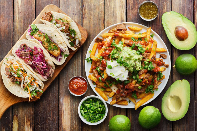 Aerial view of four tacos, carne asada fries, avocado, lemon and other toppings