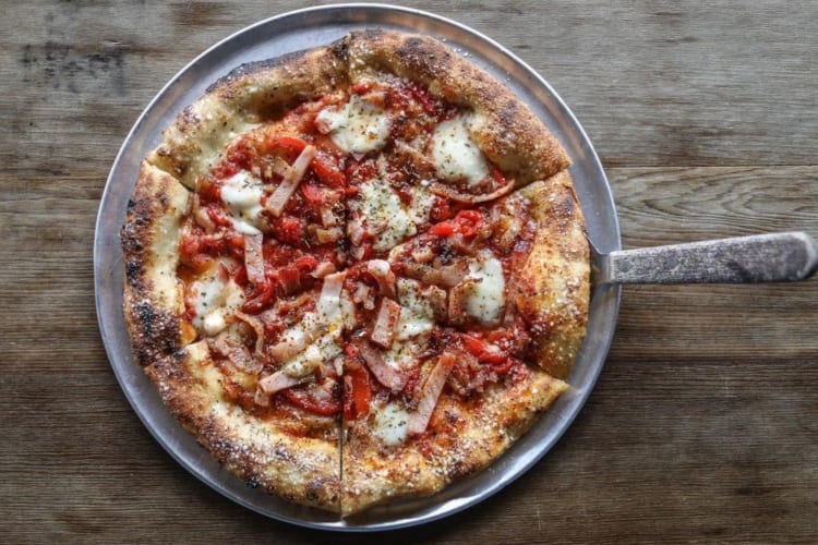 A pizza with tomato sauce, mozzarella, bacon and roasted red pepper